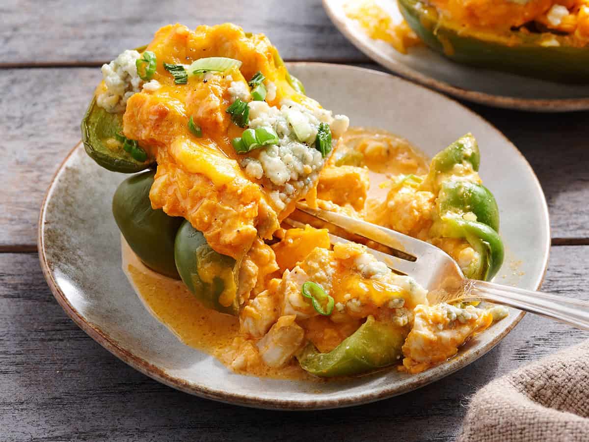 Vue latérale d'un poivron farci au poulet Buffalo coupé en deux sur une assiette.
