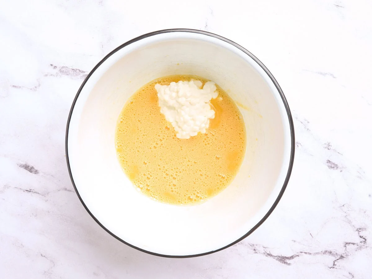Œufs battus dans un bol avec du fromage cottage ajouté.