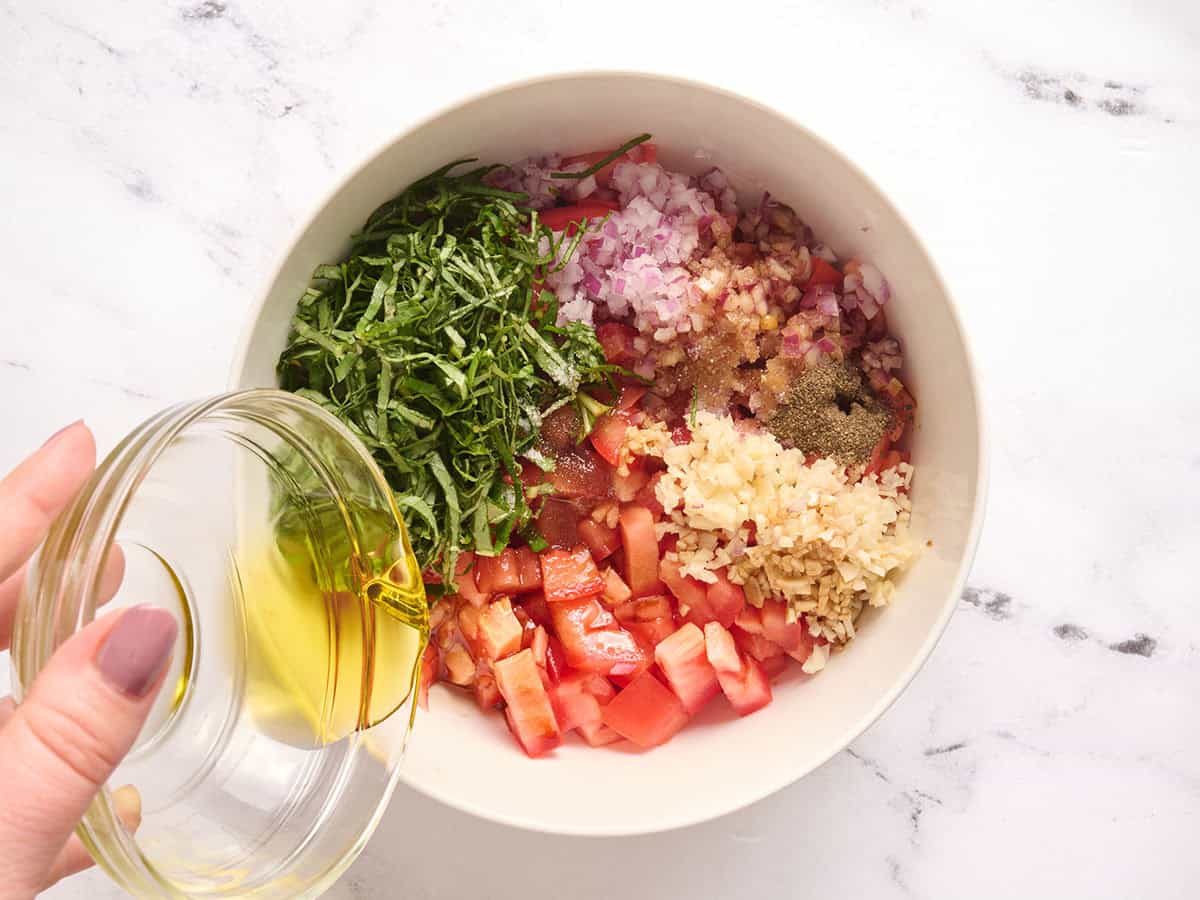 Tomates en dés, basilic frais tranché, oignon rouge coupé en dés, assaisonnements, ail émincé dans un bol avec de l'huile d'olive versée.