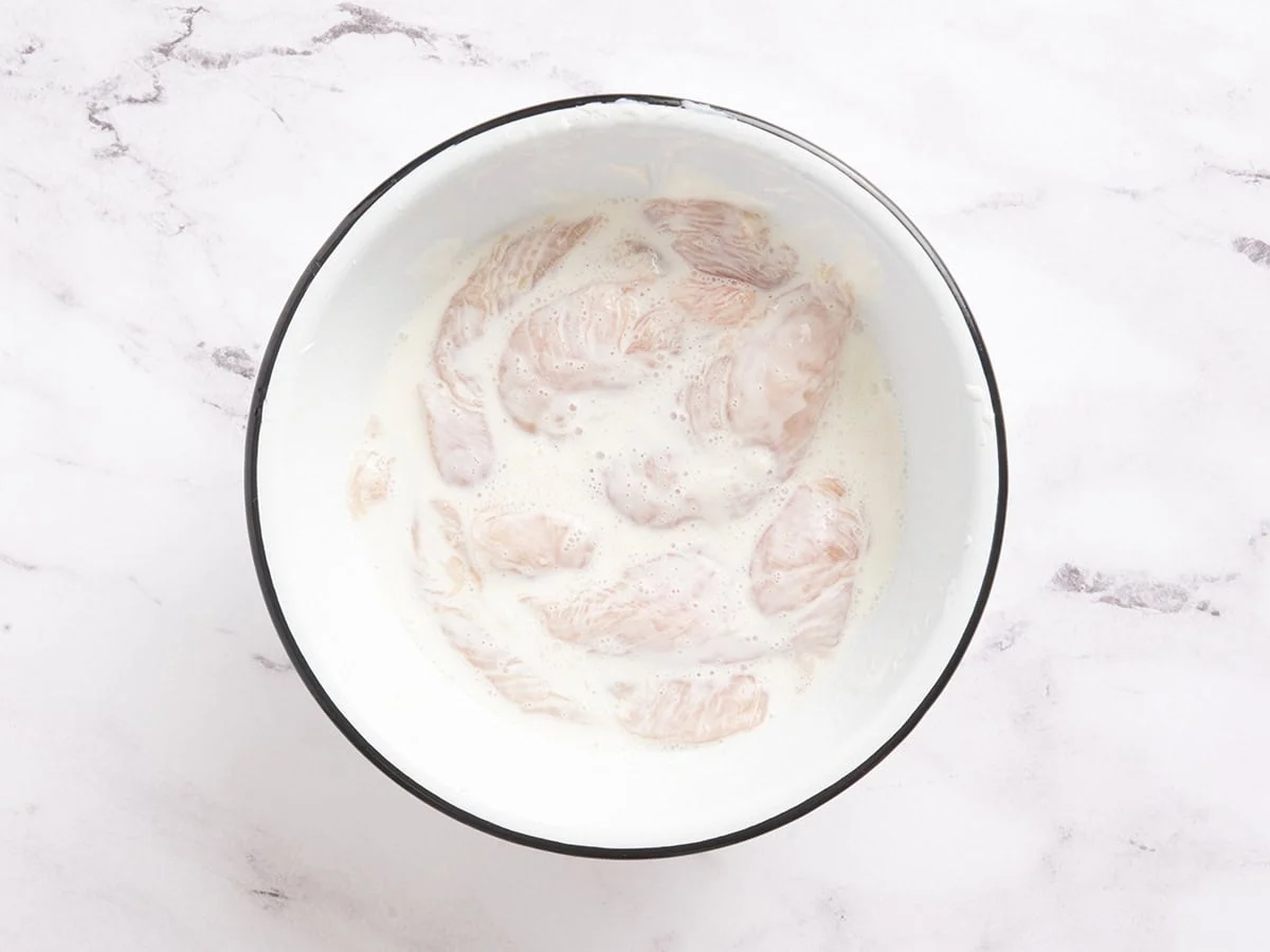 Filets de poulet dans un bol avec du yaourt et de l'eau.