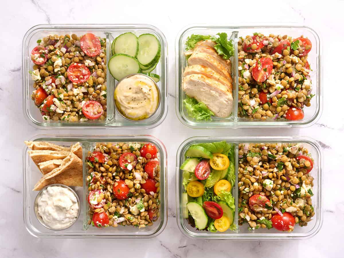 Vue aérienne de quatre récipients de préparation de repas avec salade de lentilles, sauce tzatziki, tranches de concombre et poulet grillé.