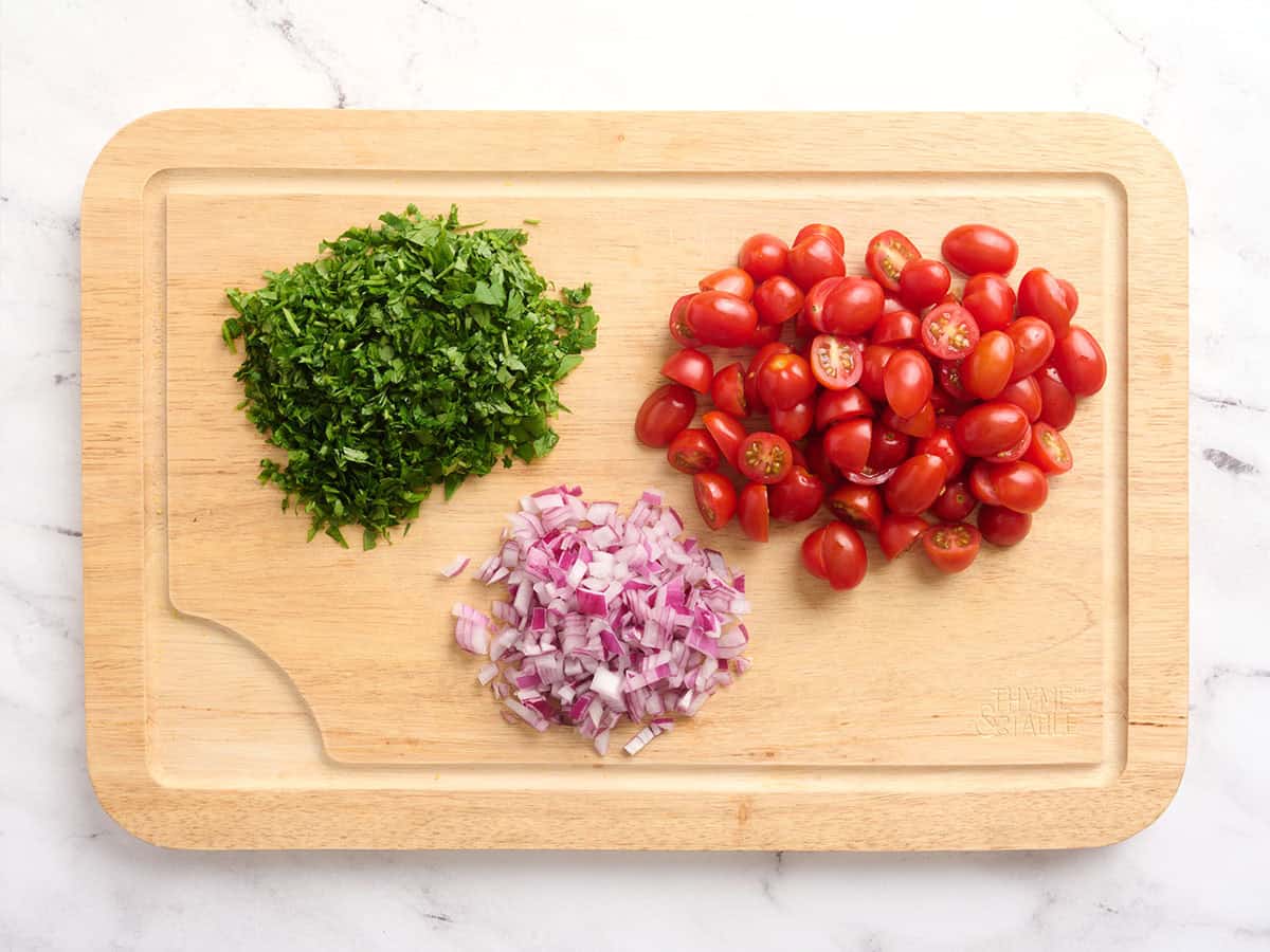 Tomates hachées, persil et oignon rouge sur une planche à découper.