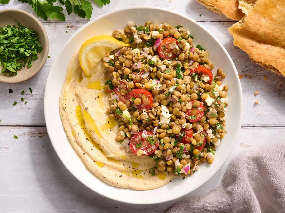 Un bol de houmous avec une salade de lentilles et un quartier de citron.