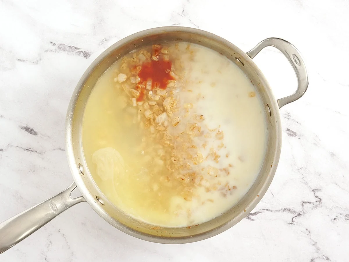 Bouillon de poulet, lait et sauce piquante ajoutés dans une poêle avec des oignons.