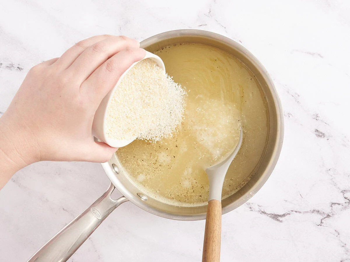 Du gruau est versé dans de l'eau et du bouillon de poulet dans une casserole.