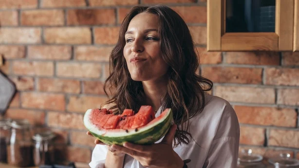 Femme à la maison mangeant de la pastèque dans la cuisine.