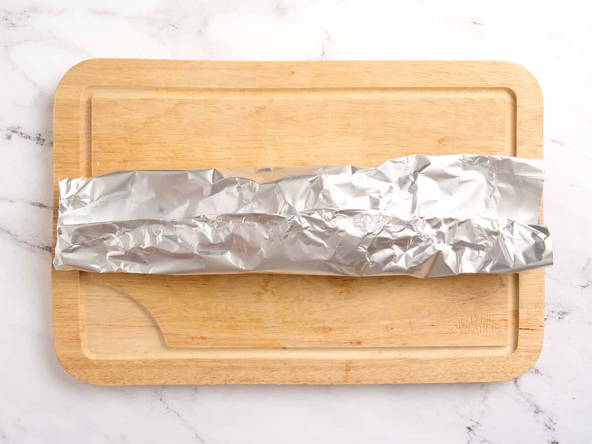 Un paquet de papier d'aluminium plié en deux sur une planche à découper en bois.
