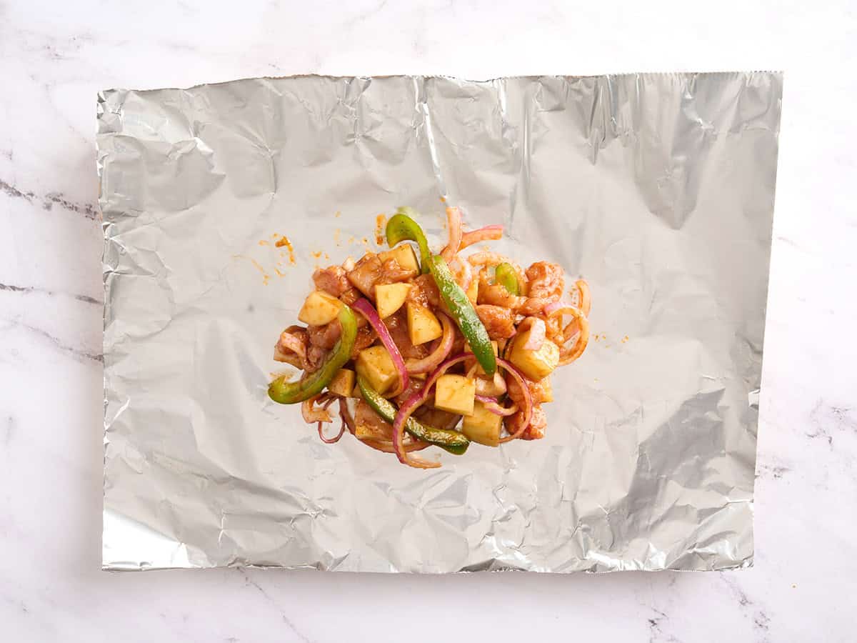 Poulet BBQ, pommes de terre, poivrons et oignons sur une feuille de papier d'aluminium.