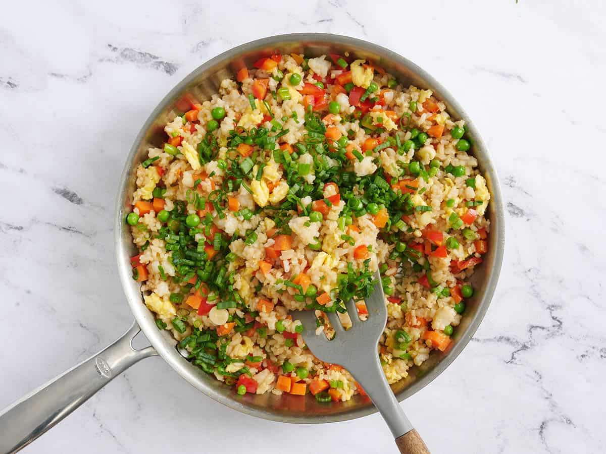 Oignons verts mélangés à du riz aux légumes dans une poêle.