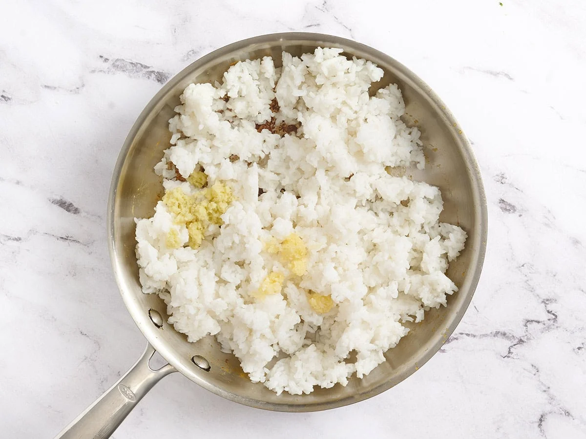 Gingembre et ail ajoutés à une poêle avec du riz.