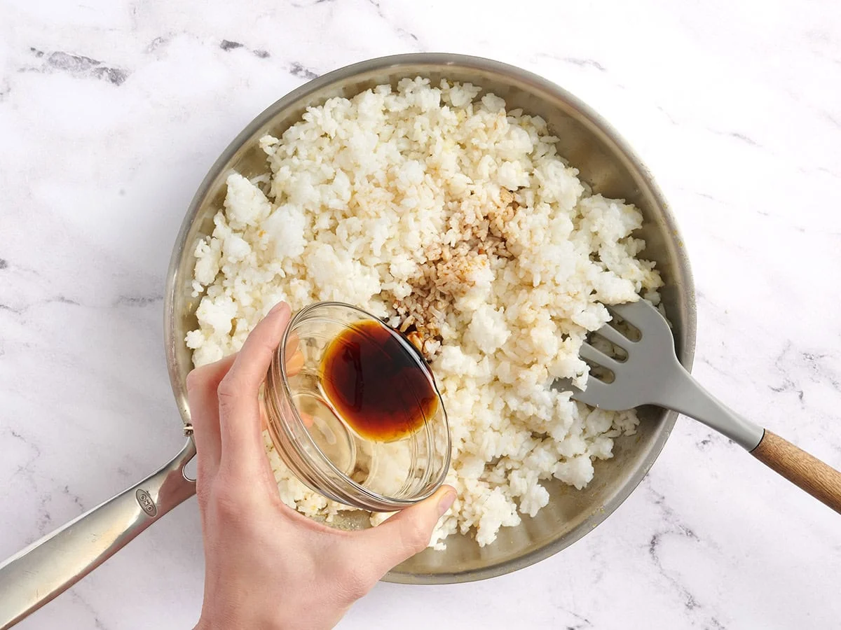 Huile de sésame et sauce soja ajoutées à une poêle de riz.