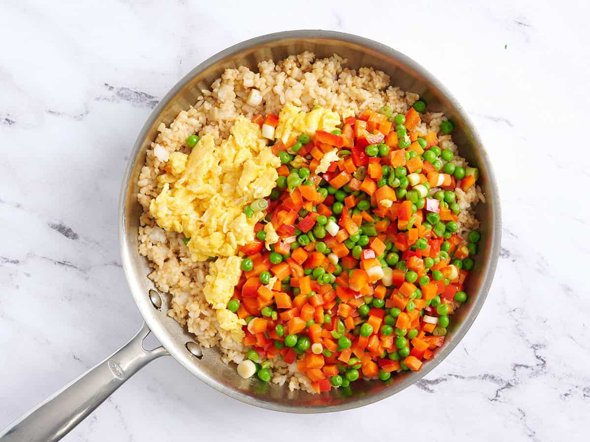 Oeufs brouillés et légumes ajoutés au riz frit dans une poêle.