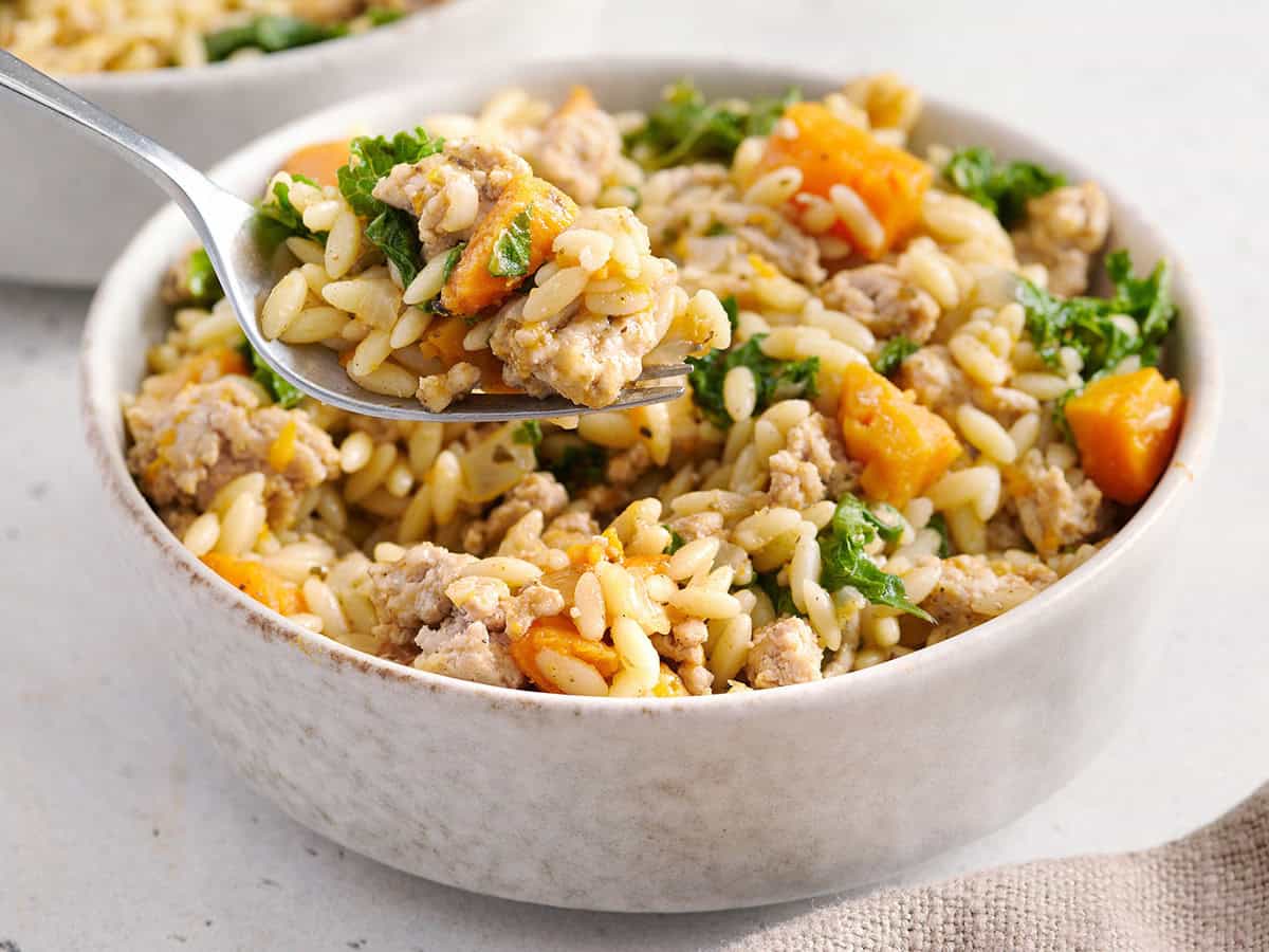 Vue latérale de la patate douce et de l'orzo de dinde hachée dans un bol avec un couteau en prenant.