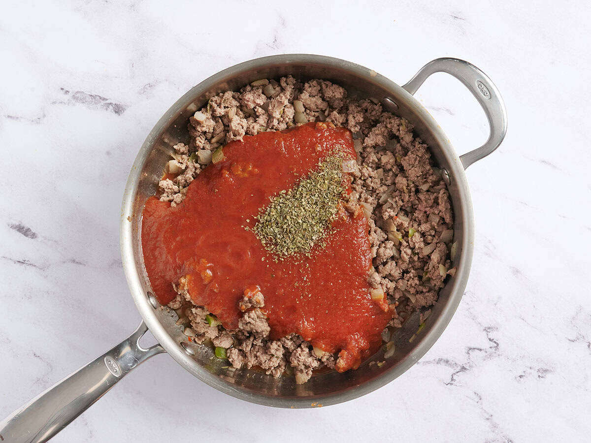 Sauce marinara ajoutée à une poêle avec assaisonnement italien et viande hachée dorée.