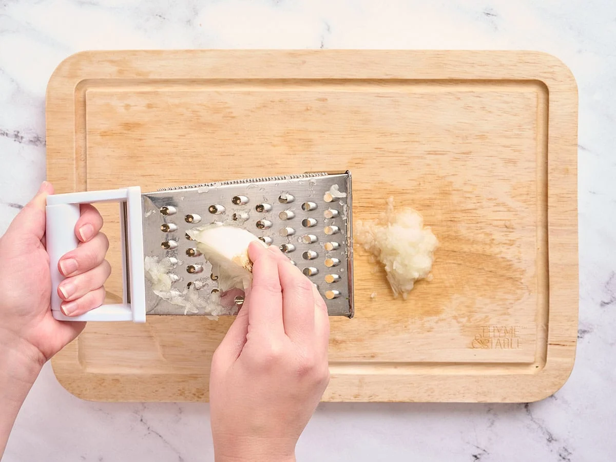 Mains utilisant une râpe à fromage pour râper un oignon blanc.