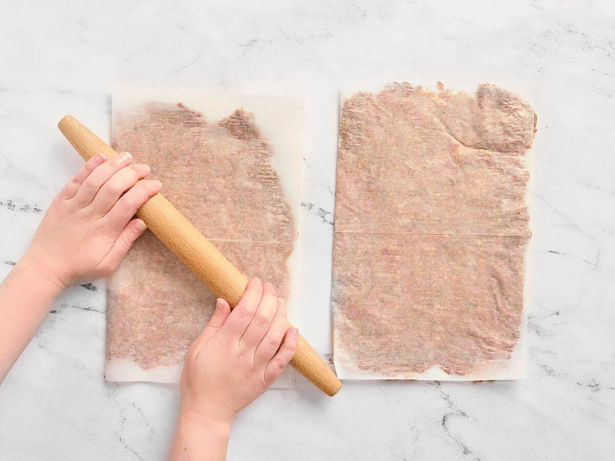 Aplatir le bœuf haché entre deux morceaux de papier sulfurisé avec les mains à l'aide d'un rouleau à pâtisserie jusqu'à ce qu'il soit aplati.