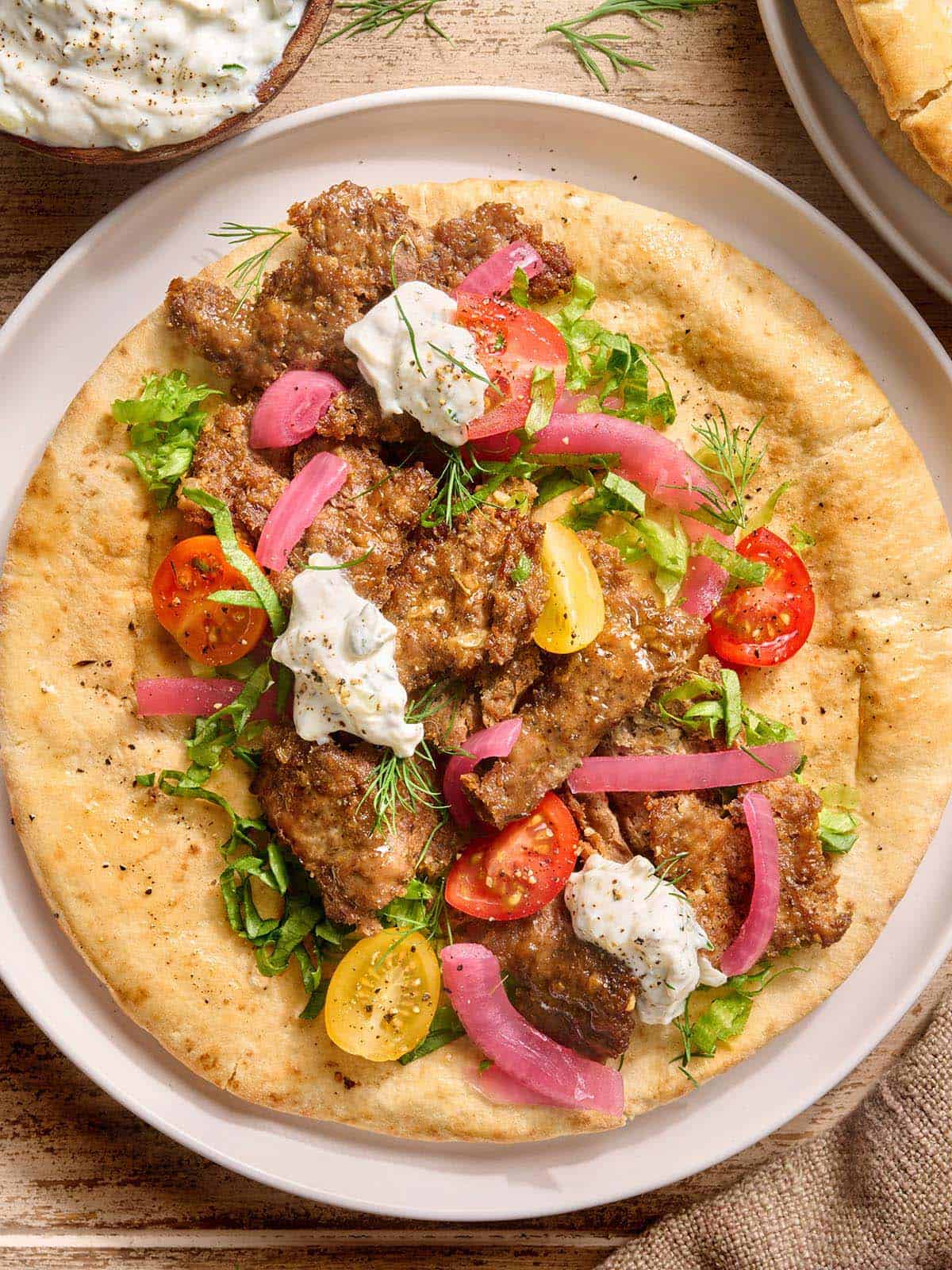 Vue aérienne d'un doner kebab sur une plaque de pain pita avec salade et sauce tzatziki.