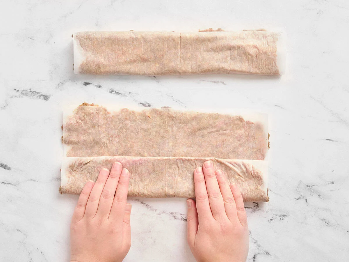Mains roulant du bœuf haché dans du papier sulfurisé.