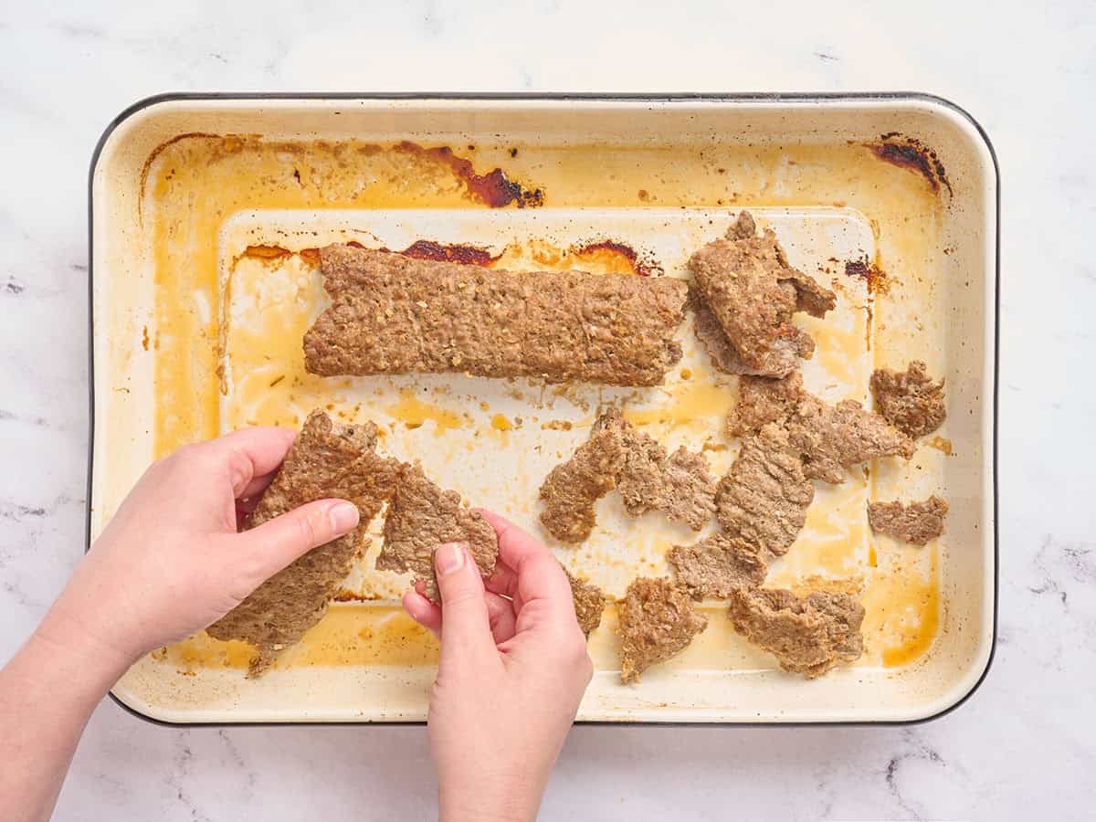 Les mains déchiquetent la plaque de cuisson pour donner la viande de kebab en petits morceaux.