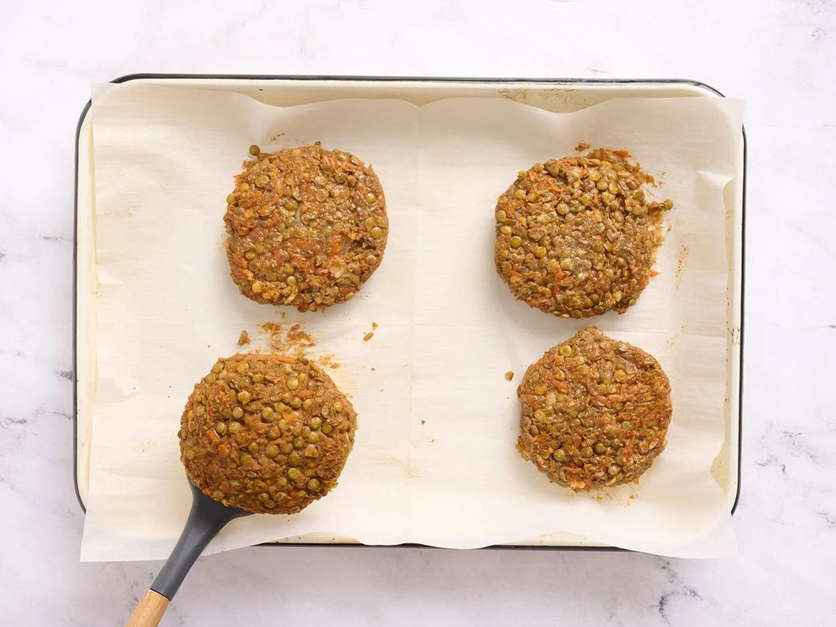 Burgers de lentilles sur une plaque de cuisson retournés à mi-cuisson avec une spatule.