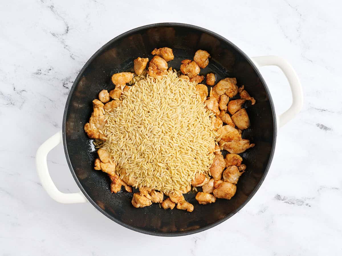 Orzo non cuit ajouté à une poêle avec du poulet cuit.