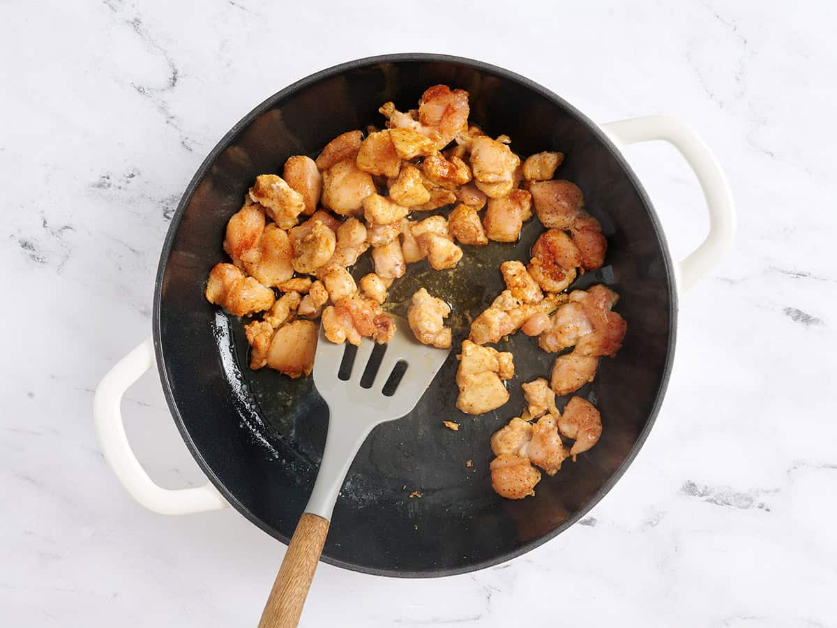 Une spatule retournant les morceaux de poulet dans une poêle.