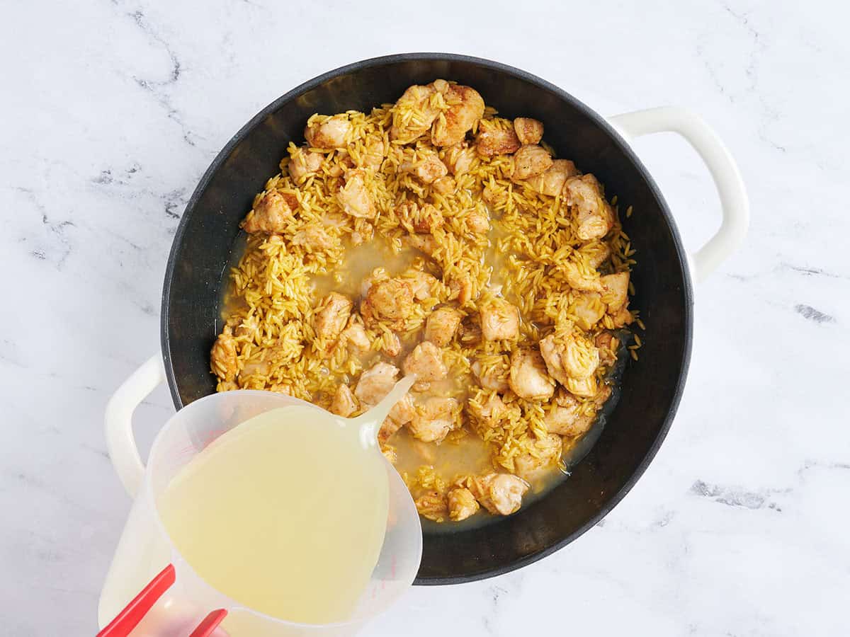 Bouillon versé dans une poêle avec du poulet cuit et de l'orzo grillé.