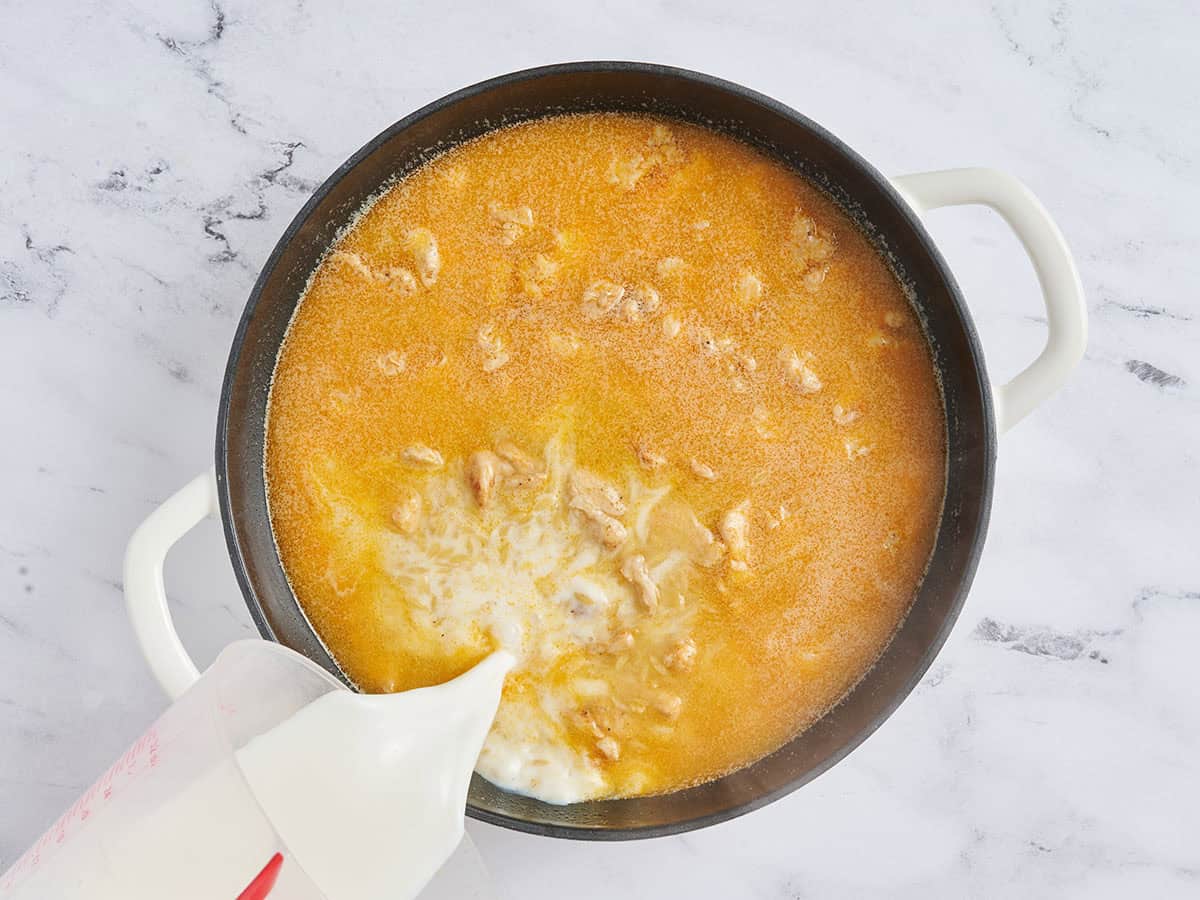 Lait versé dans une poêle avec l'orzo, le poulet et le bouillon.