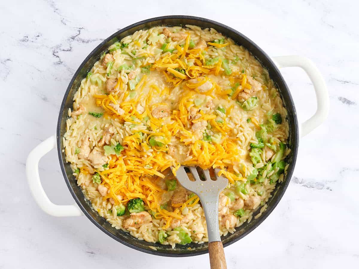 Cheddar râpé mélangé à une casserole de poulet et de brocoli.