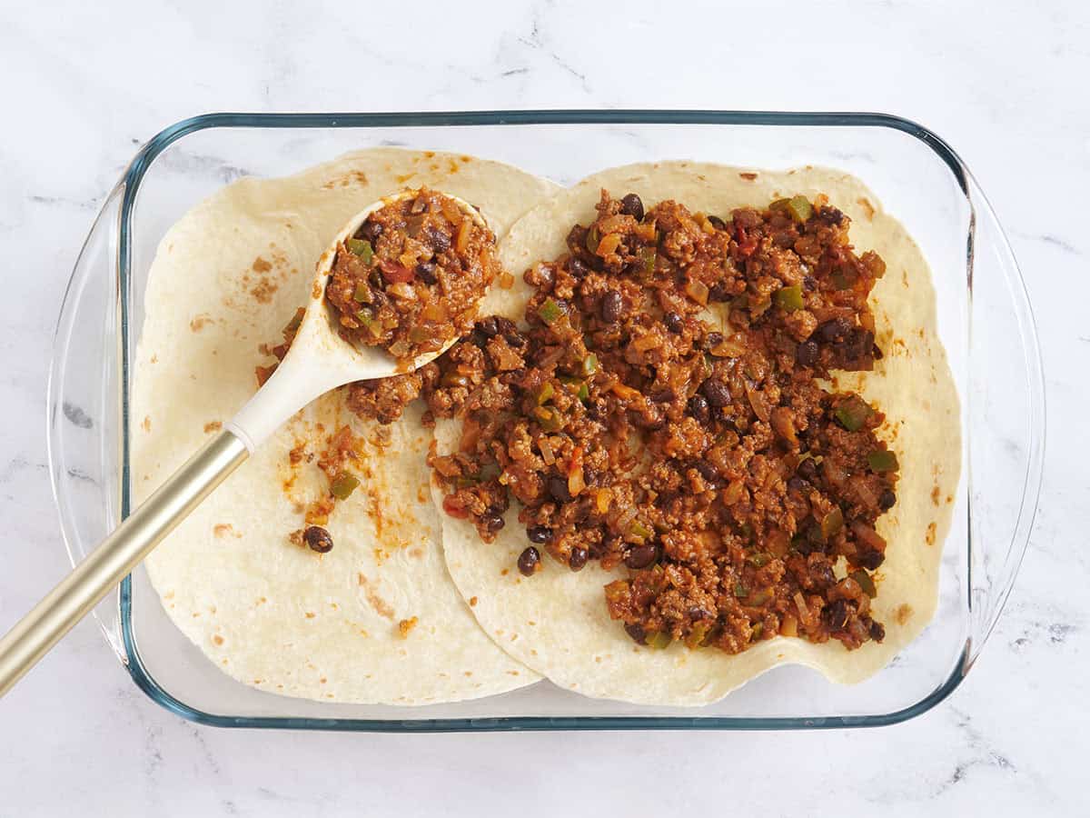 Tortillas disposées dans un plat allant au four avec de la viande à tacos superposée.