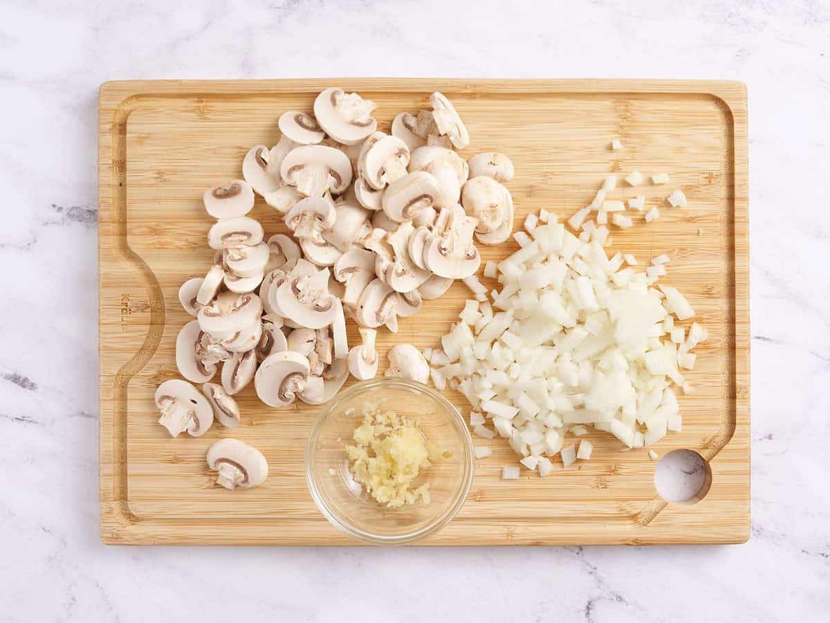 Champignons tranchés, oignons coupés en dés et ail émincé sur une planche à découper.