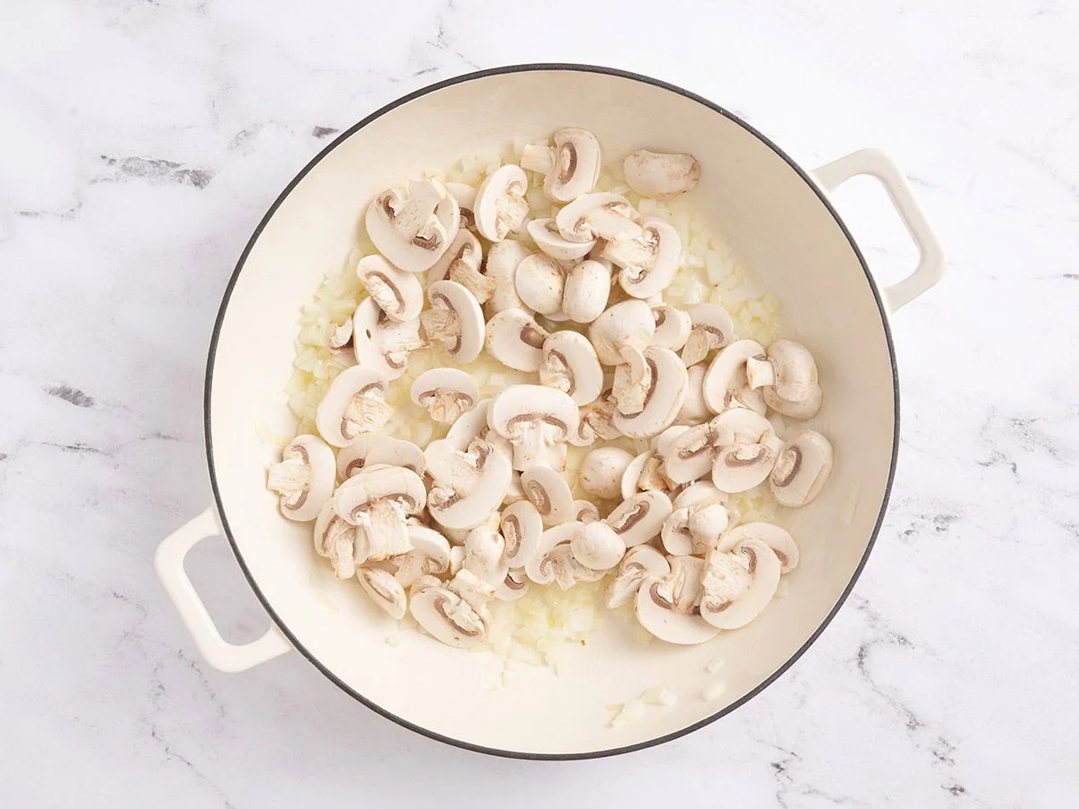Champignons ajoutés à une poêle avec des oignons sautés.