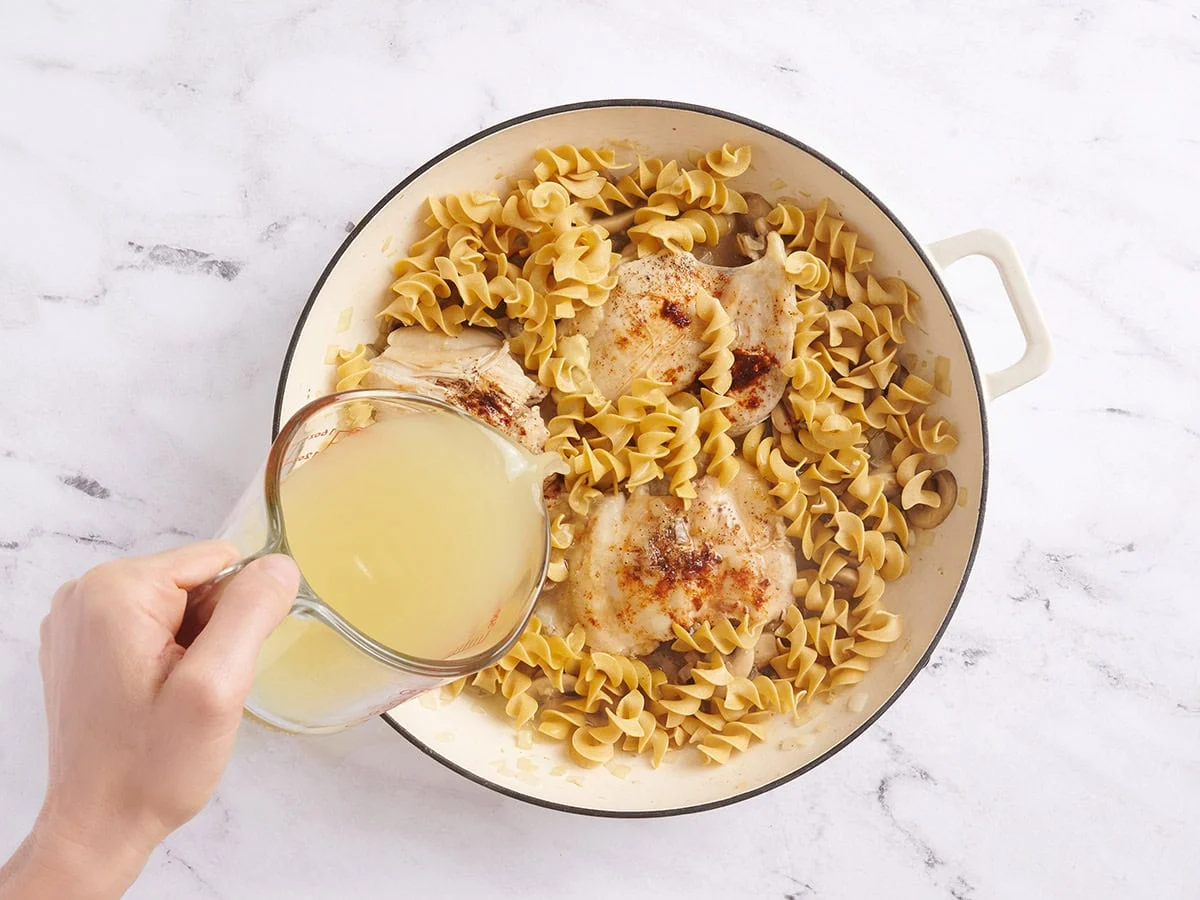 Nouilles dans une poêle avec des cuisses de poulet et des champignons, versées avec du bouillon.