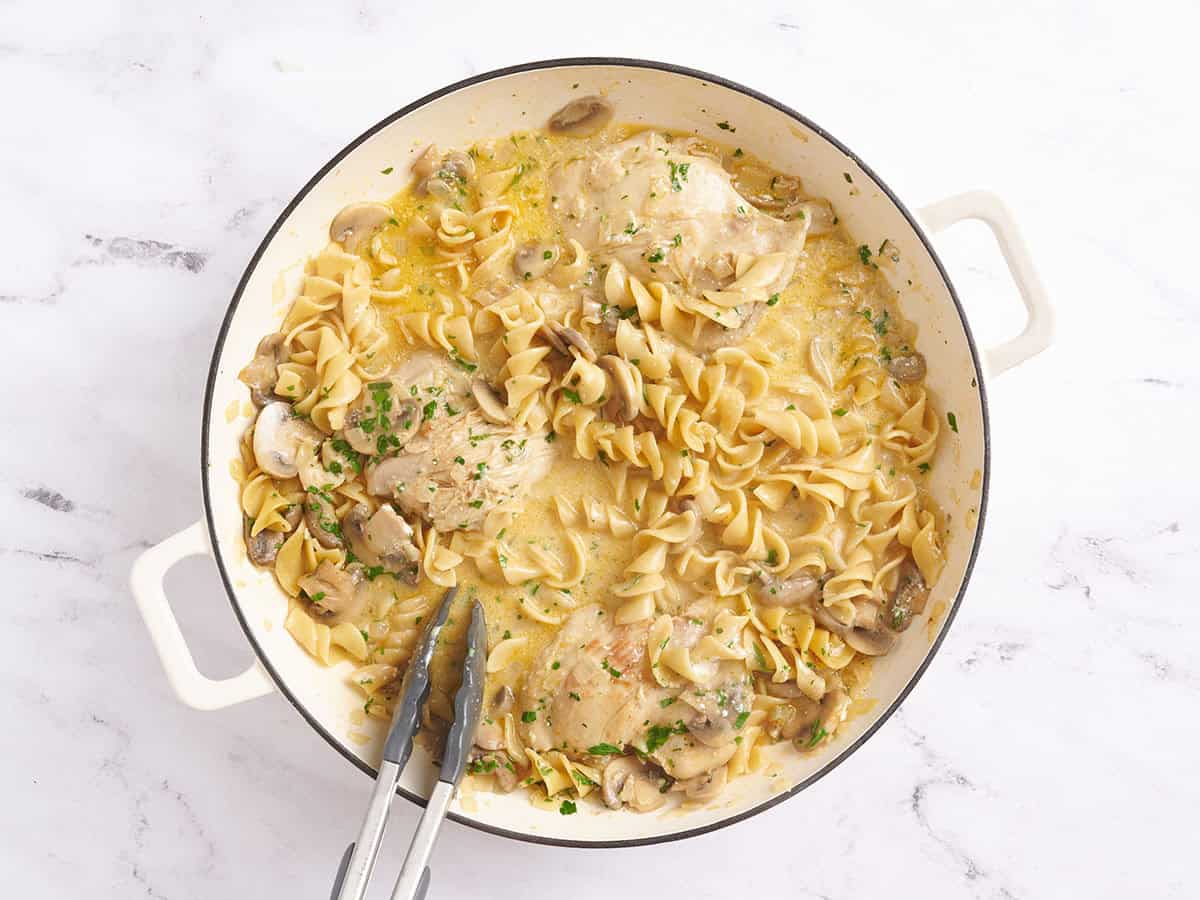 Poulet Stroganoff dans une poêle avec des pinces de cuisine.