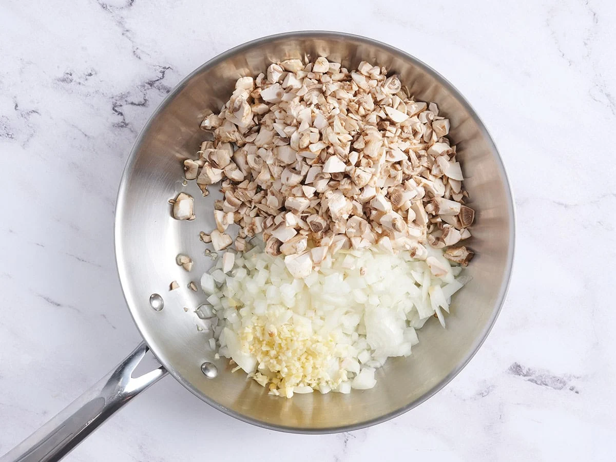 Oignons coupés en dés, champignons et ail émincé dans une poêle.