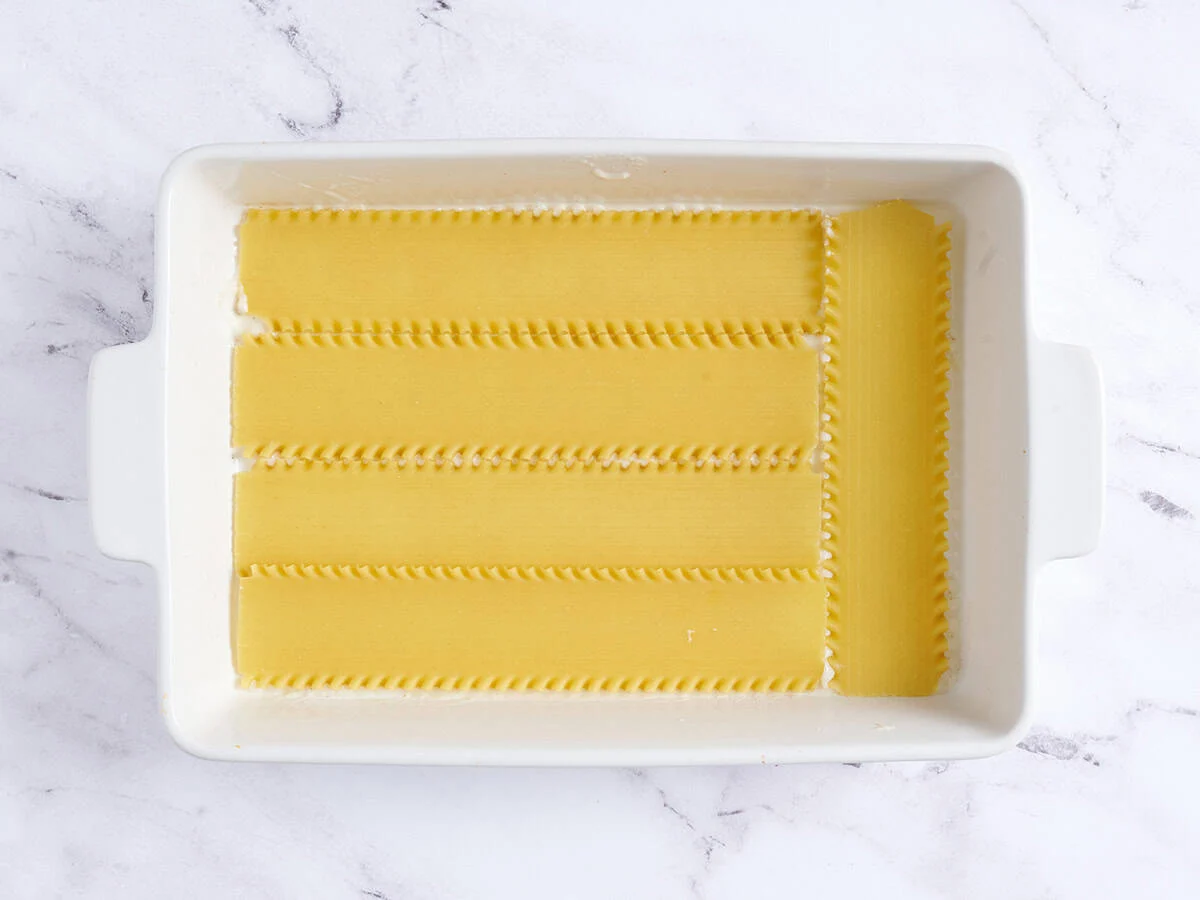 Une couche de nouilles à lasagne ajoutée à un plat allant au four.
