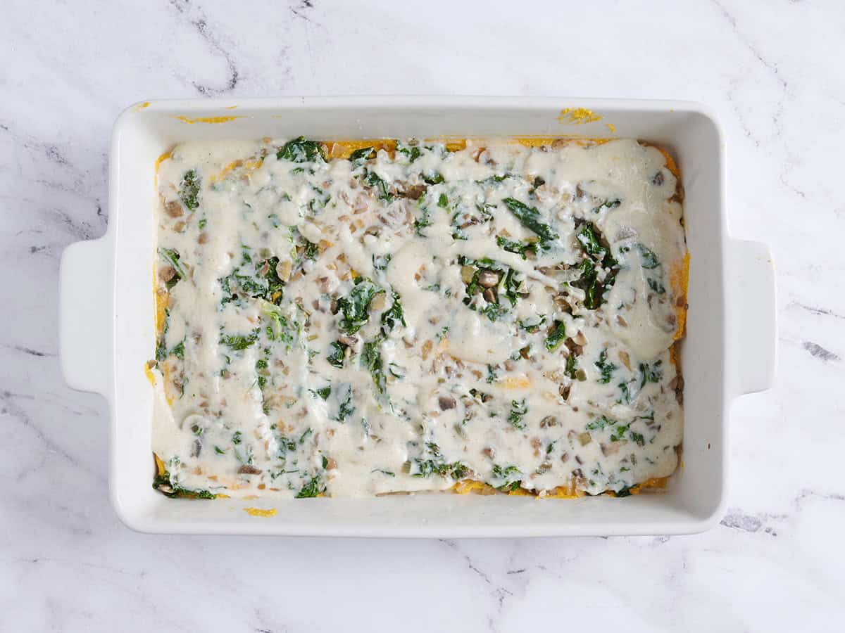 Une autre couche de sauce béchamel ajoutée sur la garniture aux champignons et au chou frisé pour une lasagne à la courge musquée.