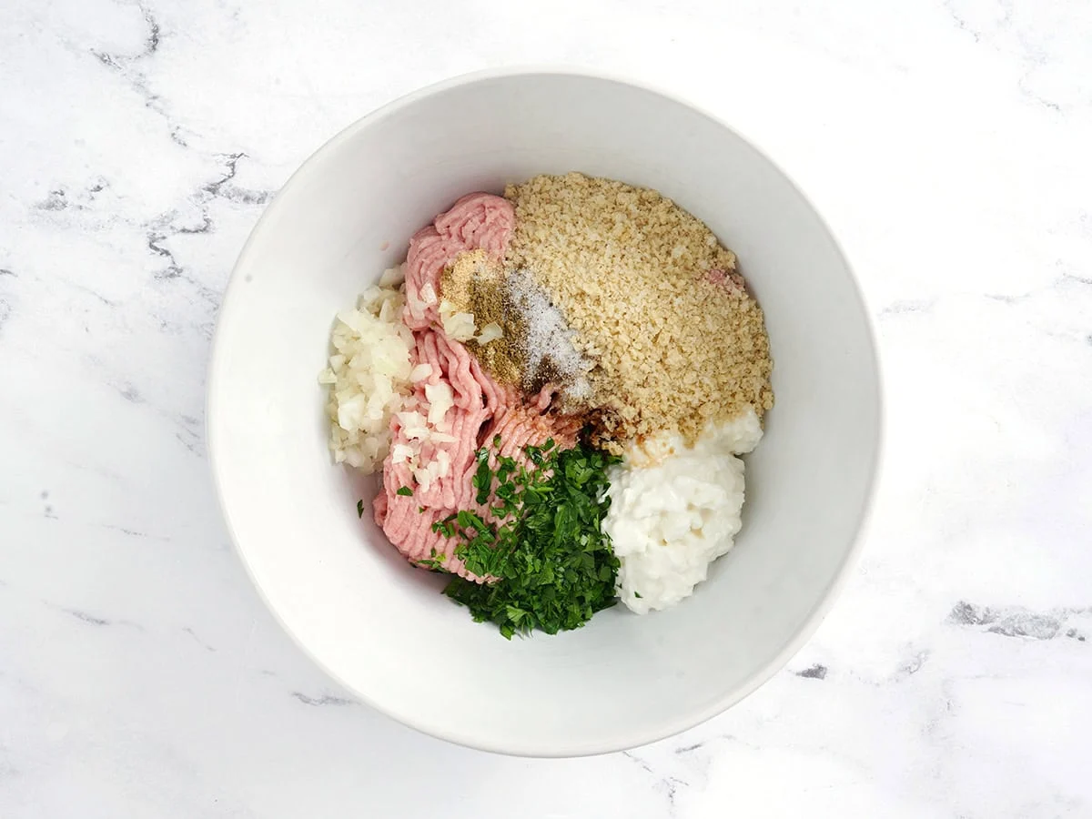 Dinde hachée, chapelure panko, fromage cottage, persil frais et oignon coupé en dés dans un bol.