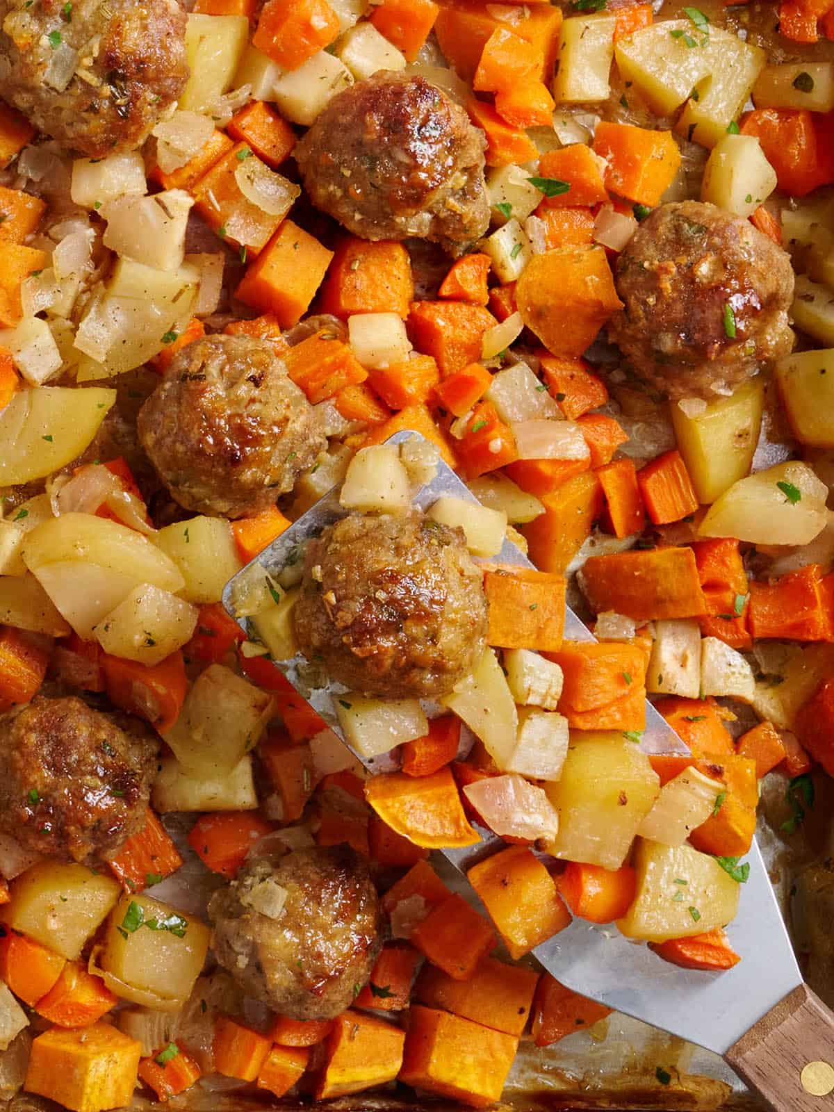 Vue aérienne des boulettes de viande de dinde et des légumes-racines avec une spatule en métal.