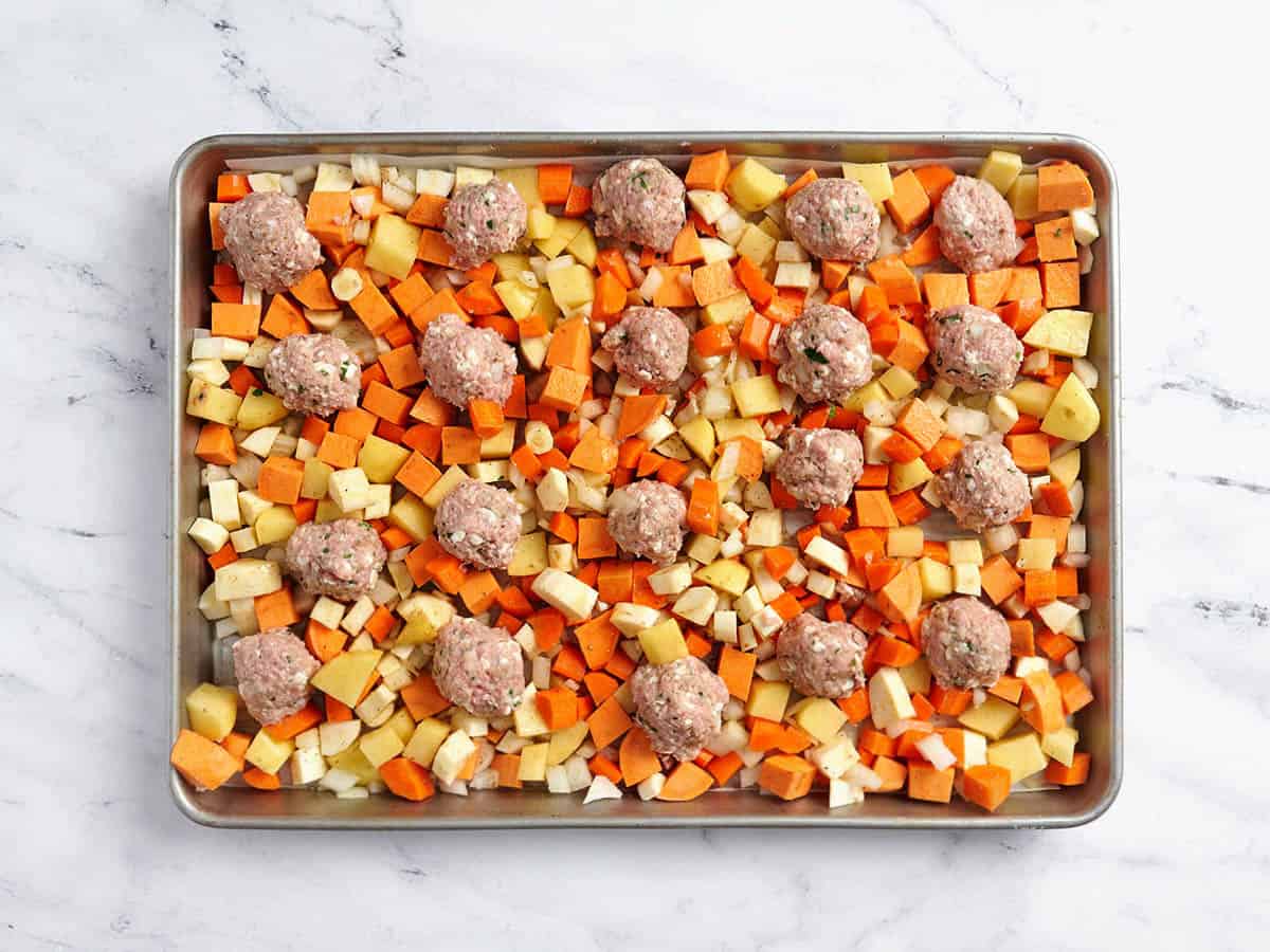 Boulettes de viande de dinde en forme ajoutées à une plaque avec des légumes-racines coupés en dés.