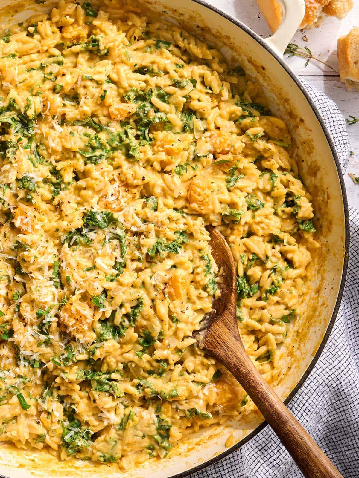 Vue rapprochée d'une poêle d'orzo crémeux à la courge musquée avec une cuillère en bois.