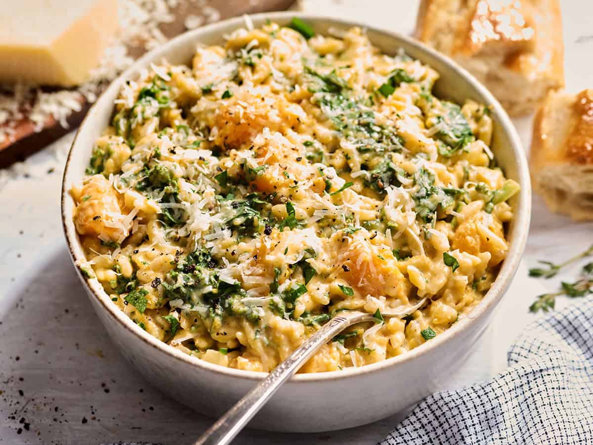 Vue latérale d'un bol d'orzo crémeux à la courge musquée avec du parmesan râpé et une fourchette.