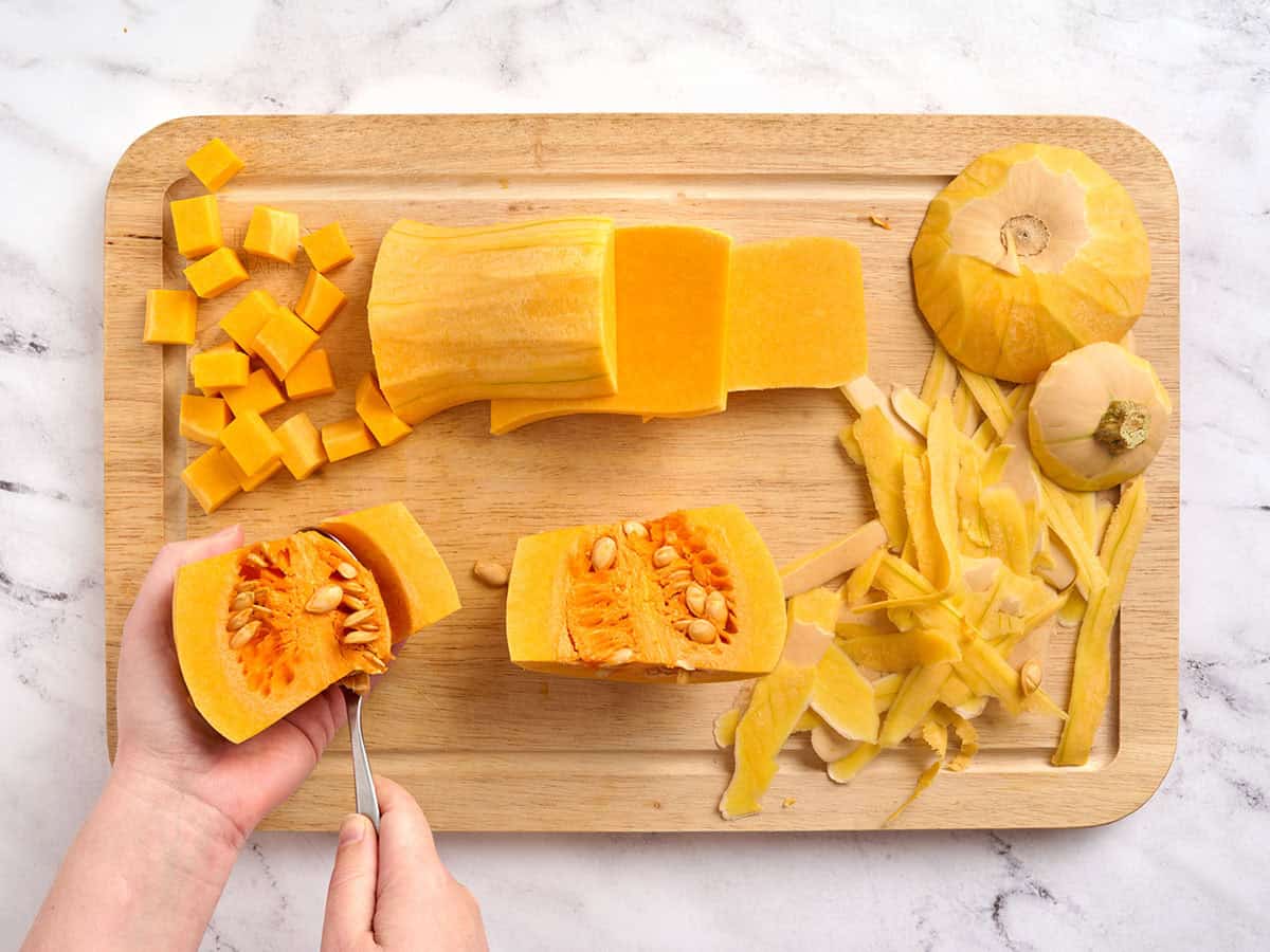 Mains préparant la courge musquée en retirant les graines, entourées de zeste de courge musquée et de courge musquée coupée en dés sur une planche à découper.