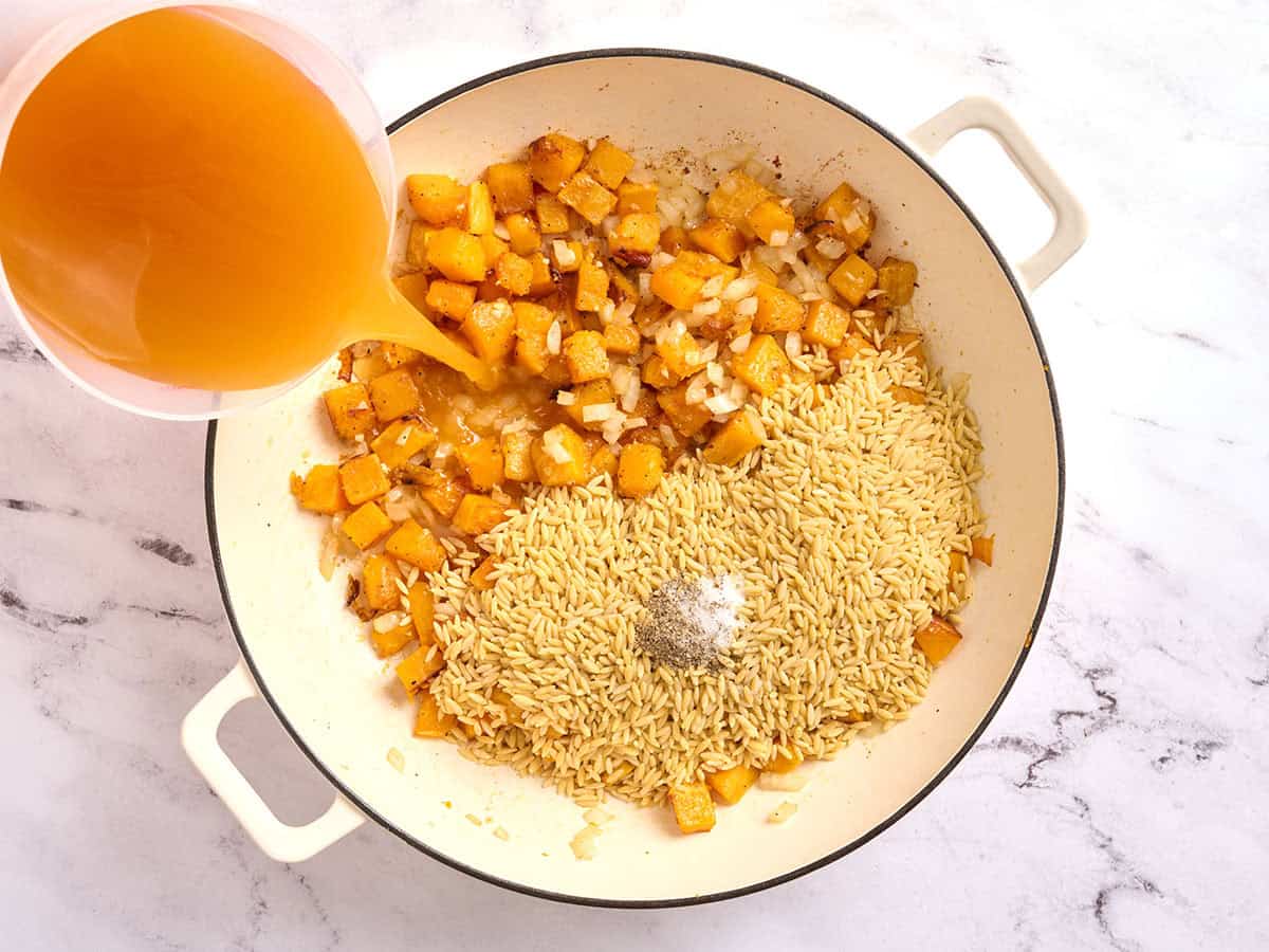 Courge musquée dans une poêle avec de l'orzo et des assaisonnements, en versant le bouillon.