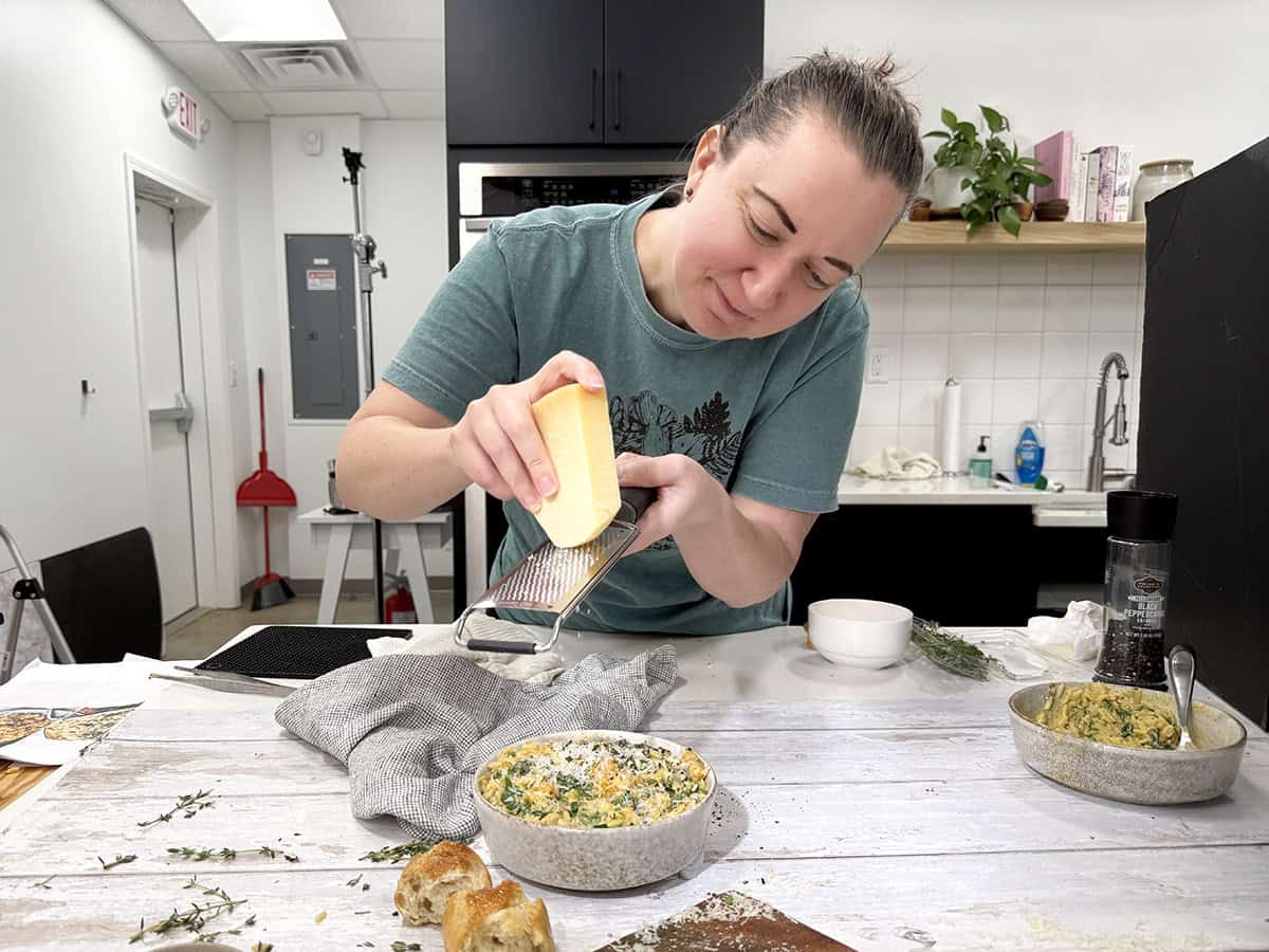 Une femme déchiquetant du parmesan frais sur un bol d'orzo de courge musquée dans une cuisine.