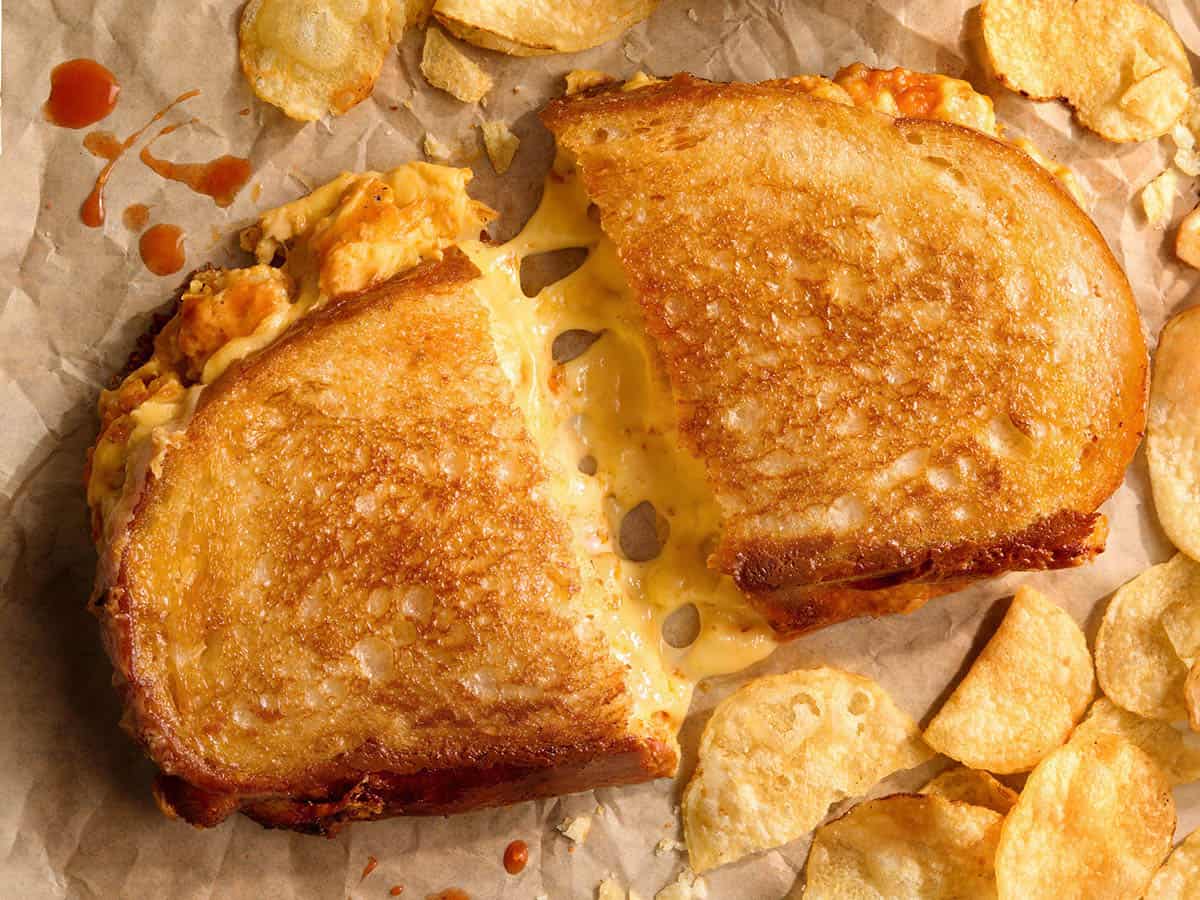Vue aérienne d'un sandwich au fromage grillé au poulet Buffalo grillé coupé en deux avec du fromage, sur du papier parchemin avec des chips.