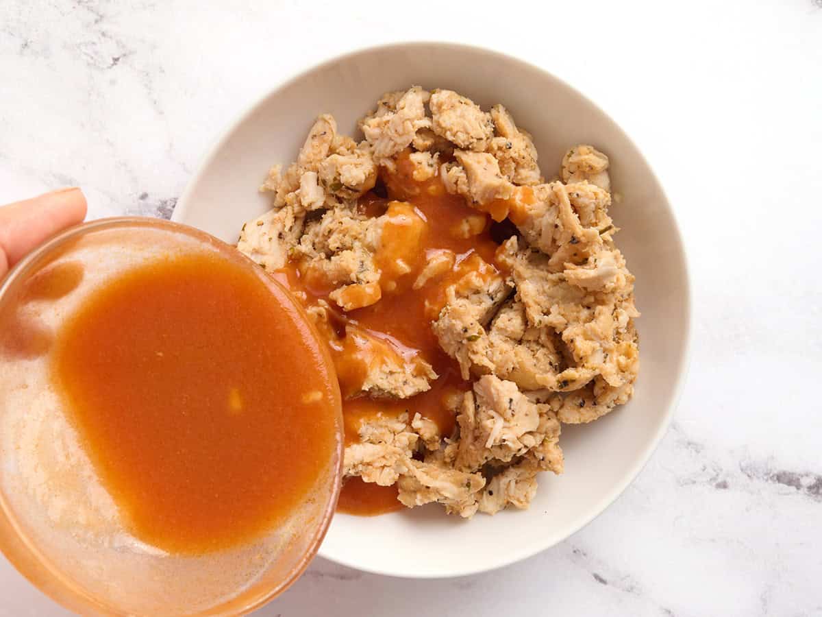 Sauce Buffalo maison versée dans un bol de poulet coupé en dés.