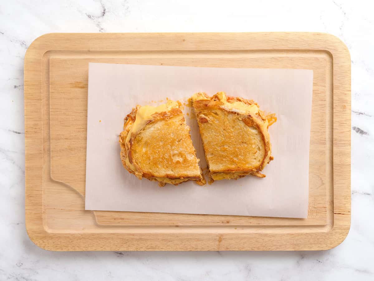 Sandwich au fromage grillé au poulet Buffalo fini coupé en deux sur une planche à découper en bois.