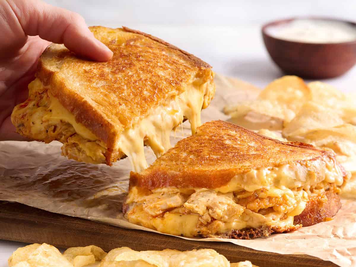 Une main prenant une demi-tranche d'un sandwich au fromage grillé au poulet Buffalo.