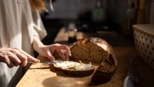 Femme étalant du beurre sur une tranche de pain de blé entier sur une planche à découper en bois